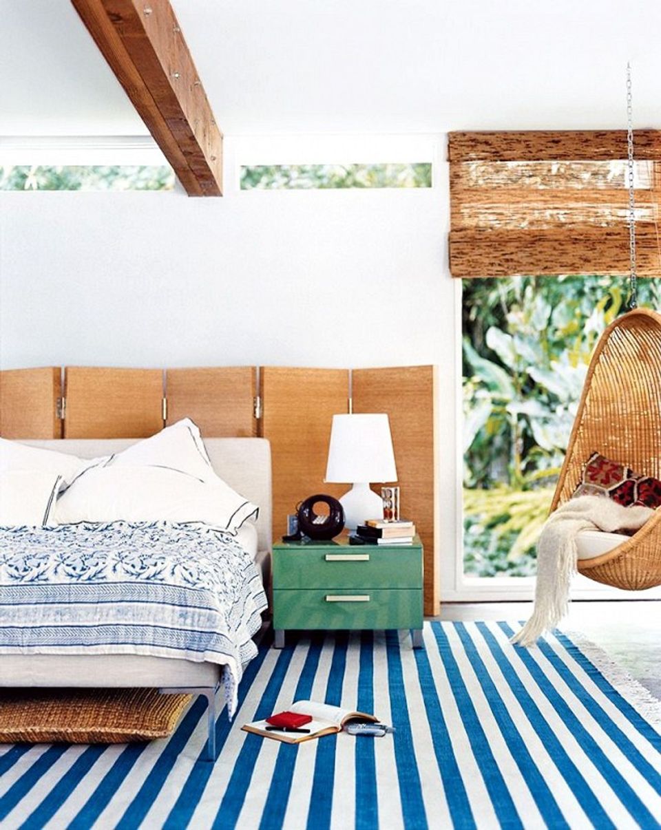 Coastal bedroom mixing warm wood tones with navy and white striped rug, relaxed beachy atmosphere.