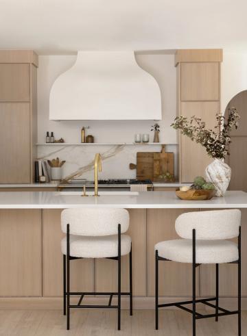 Warm minimalist kitchen with natural wood accents, marble backsplash, and brass fixtures against crisp white cabinetry