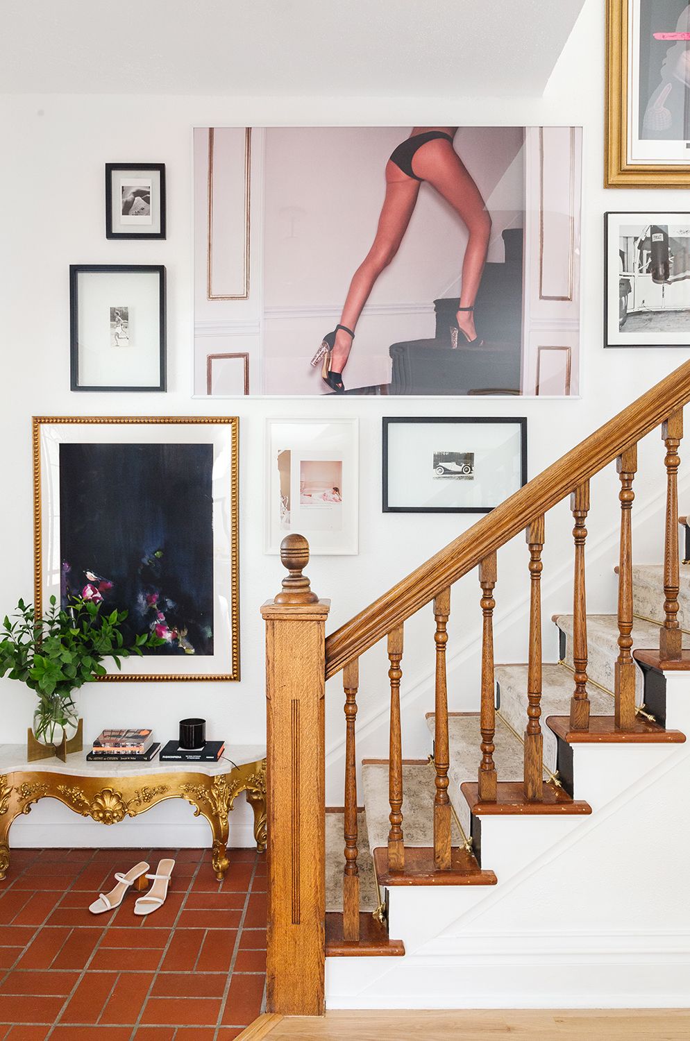 Eclectic gallery wall with mixed frames, gold accents, and bold artwork above wooden staircase railing