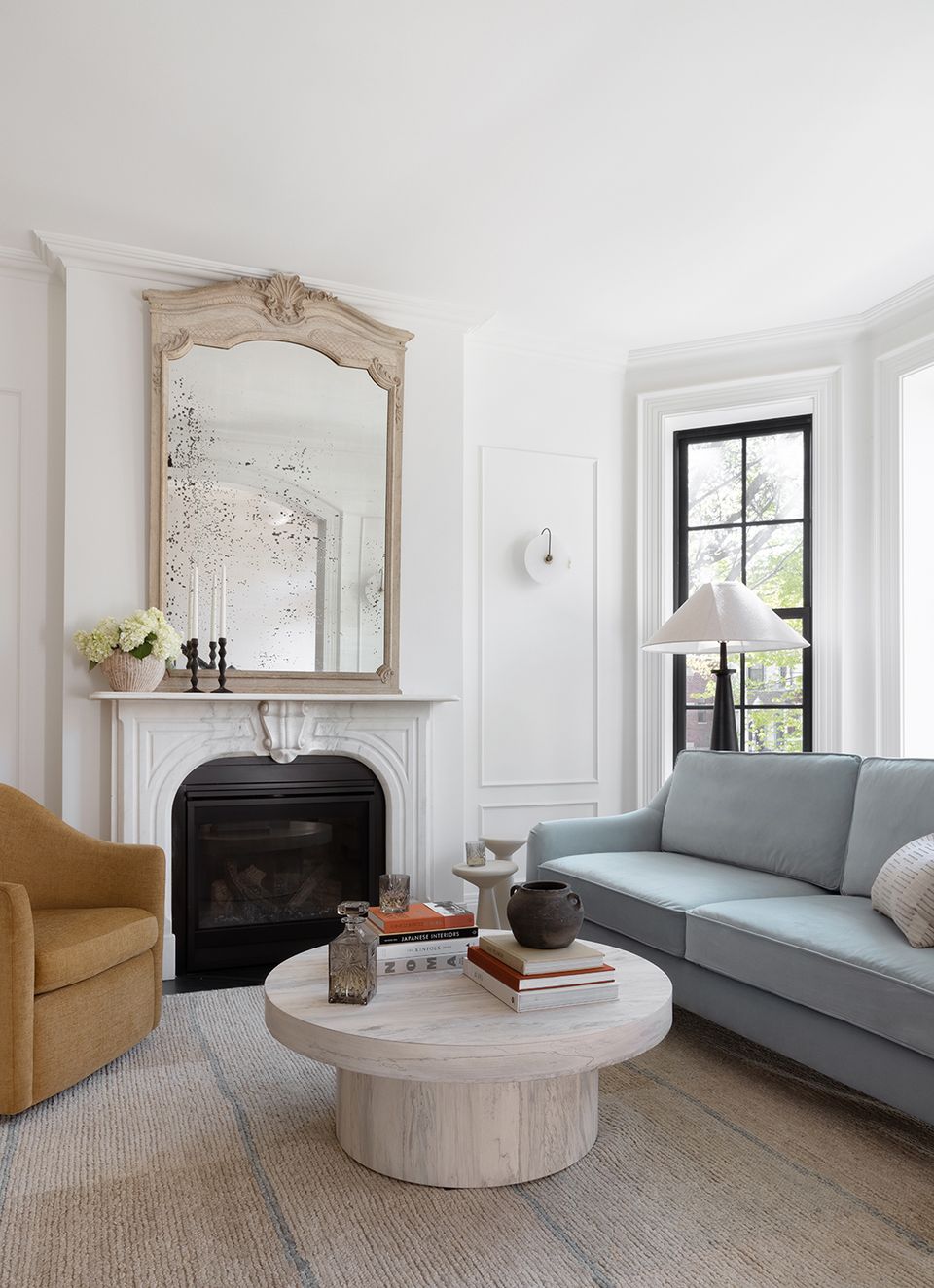 Elegant fireplace nook with gray sofa, rounded white wood table, and antique mirror above mantel