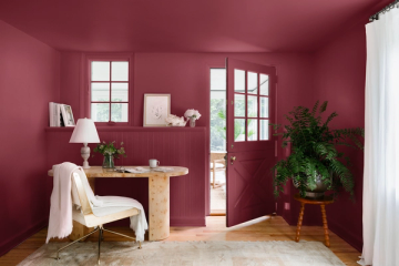 Bold jewel-tone home office with deep burgundy walls, natural wood desk, and lush greenery