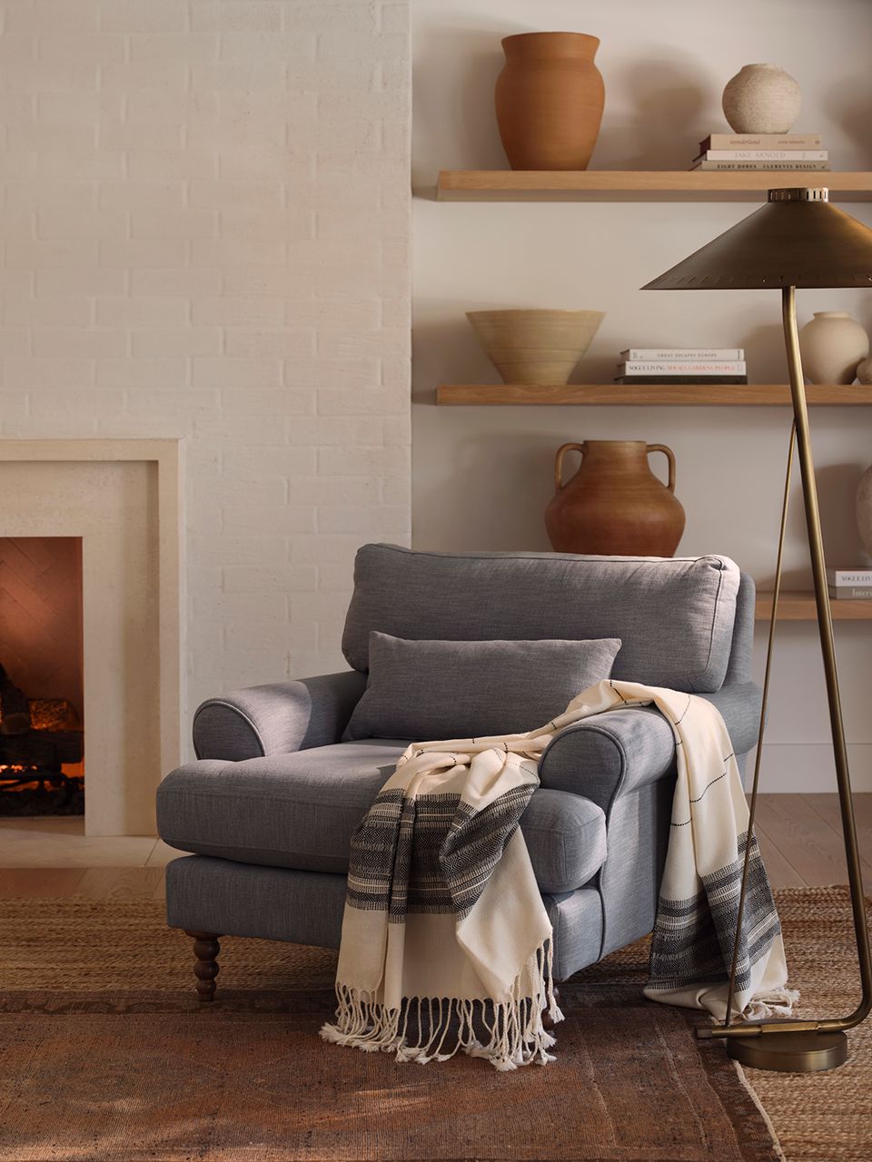 Warm earthy minimalist nook with gray armchair, terracotta pottery, and natural wood shelving