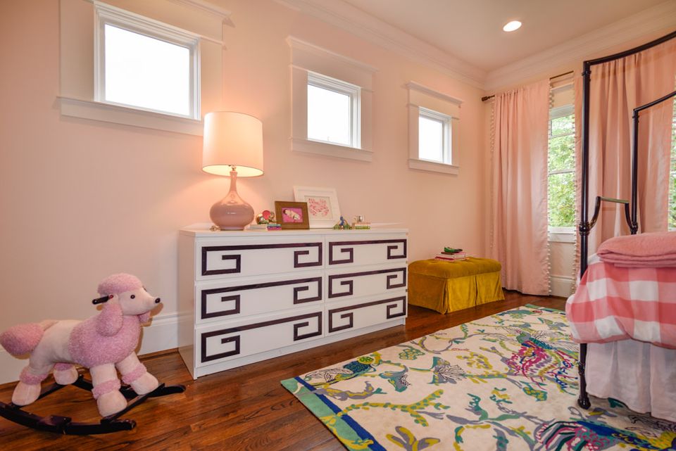 Playful child's room blending soft pink walls, geometric dresser, vibrant botanical rug, and whimsical toy accents.