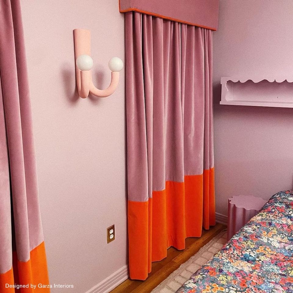 Contemporary bedroom with soft pink walls, bold color-block curtains in coral and mauve, and playful patterned bedding
