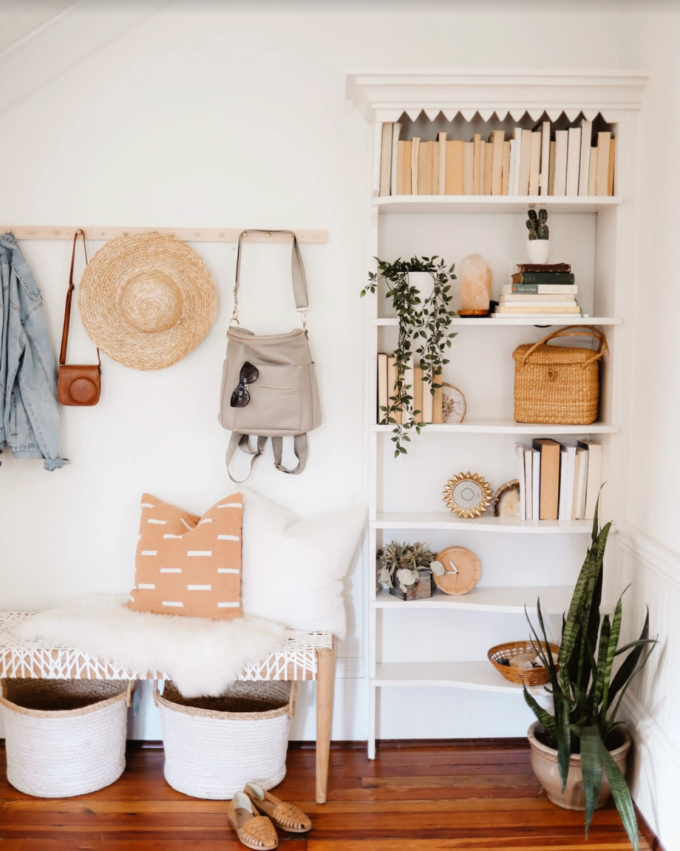 Warm, minimalist boho corner with natural wood accents, woven accessories, and curated white shelving displaying books and plants.