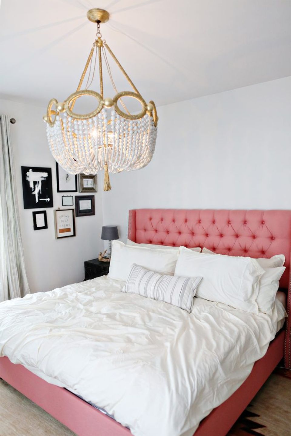 Modern bedroom featuring coral pink upholstered bed with gold crystal chandelier and gallery wall