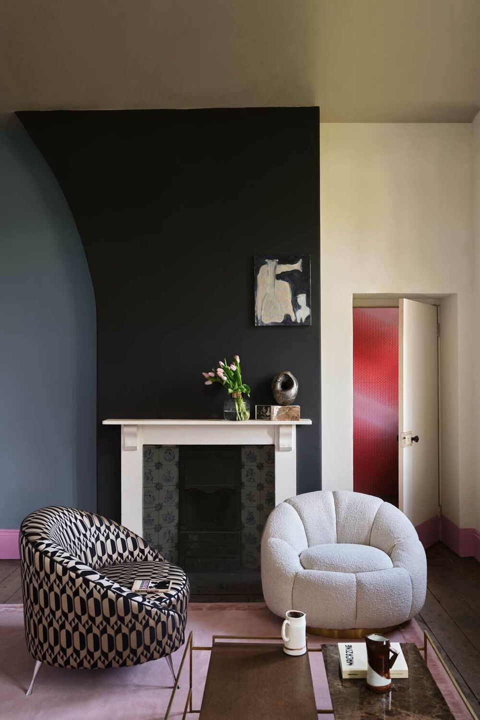 Modern living room with dark charcoal accent wall, white fireplace, curved cream armchair, and geometric patterned seating in moody, contemporary aesthetic