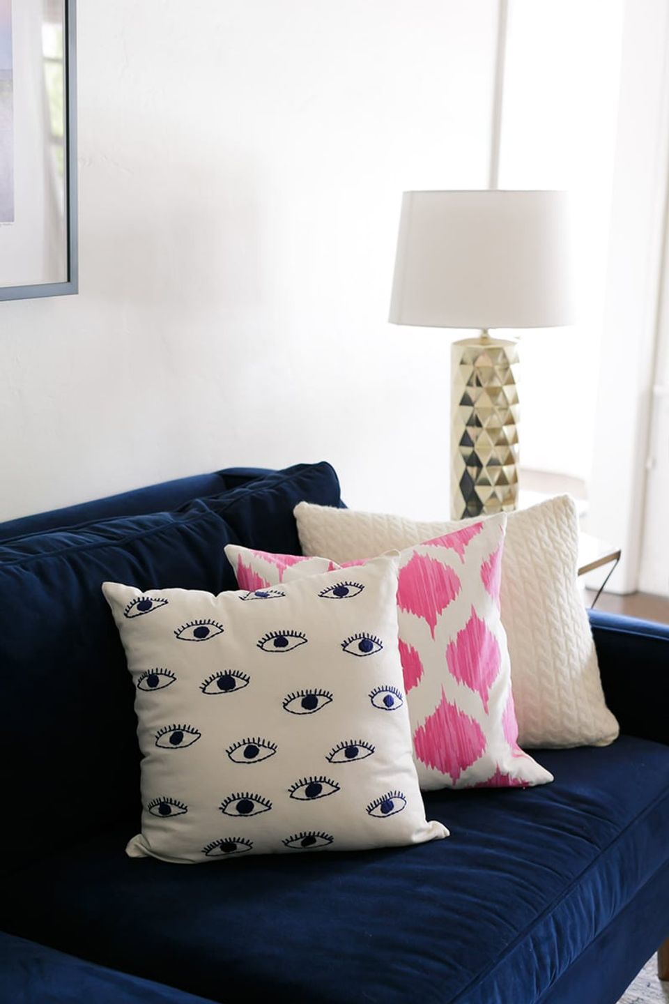 Modern navy sofa with layered patterned pillows: eye motif, pink ikat, and textured cream creating visual rhythm and repetition