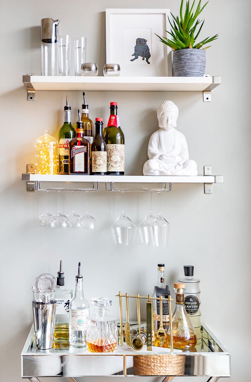 Minimalist bar cart styled with white shelving, glass and gold bottles, potted succulent, and sculptural white accent creating an elegant, curated aesthetic