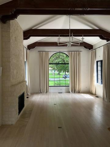 Bright farmhouse living space with exposed dark beams, cream walls, and arched window framing natural landscape views