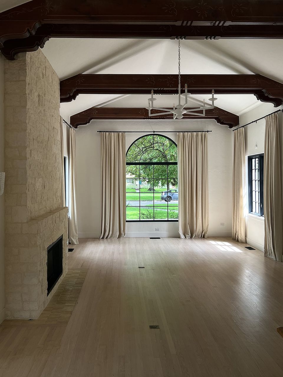 Bright farmhouse living space with exposed dark beams, cream walls, and arched window framing natural landscape views