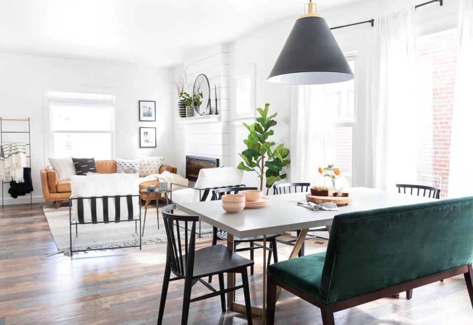 Modern farmhouse dining room with white table, black pendant light, emerald green velvet bench, and scandinavian-style chairs