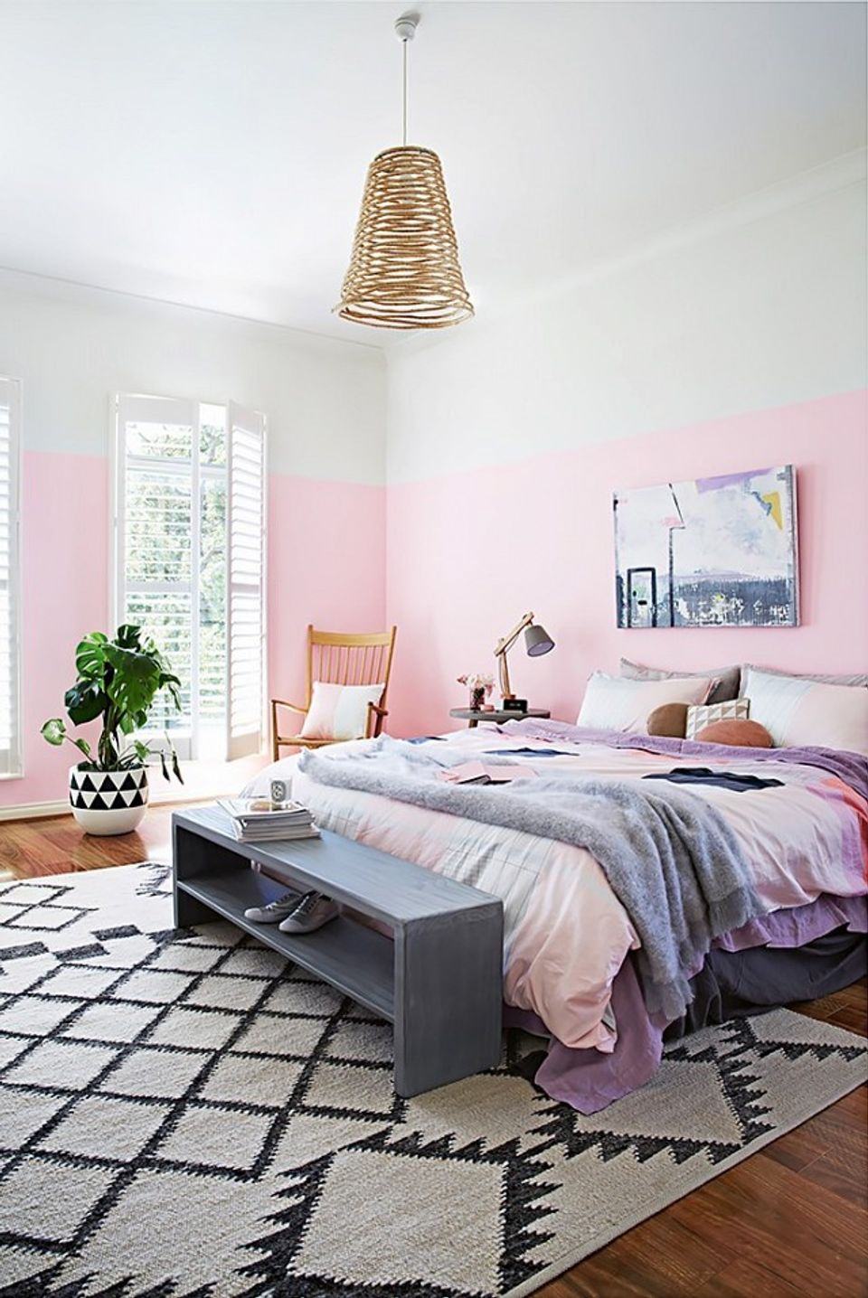 Serene bedroom with soft pink color-blocked walls, layered bedding, and natural wood accents