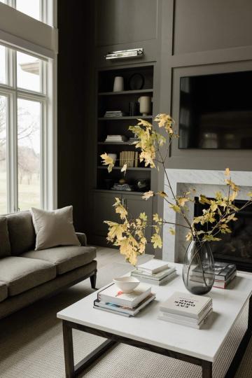 Dark moody living room with charcoal walls, black built-in shelving, white marble coffee table, and golden foliage accent