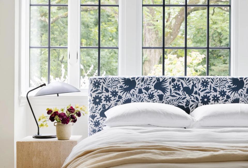 Bright minimalist bedroom featuring navy botanical print headboard, white bedding, and natural wood nightstand with fresh flowers