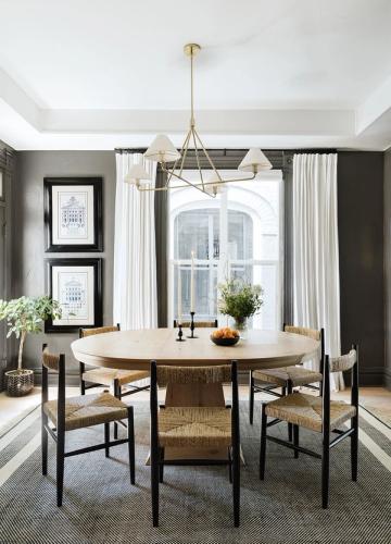 Farmhouse dining room with round wood table, brass pendant, charcoal walls, and floor-to-ceiling curtains