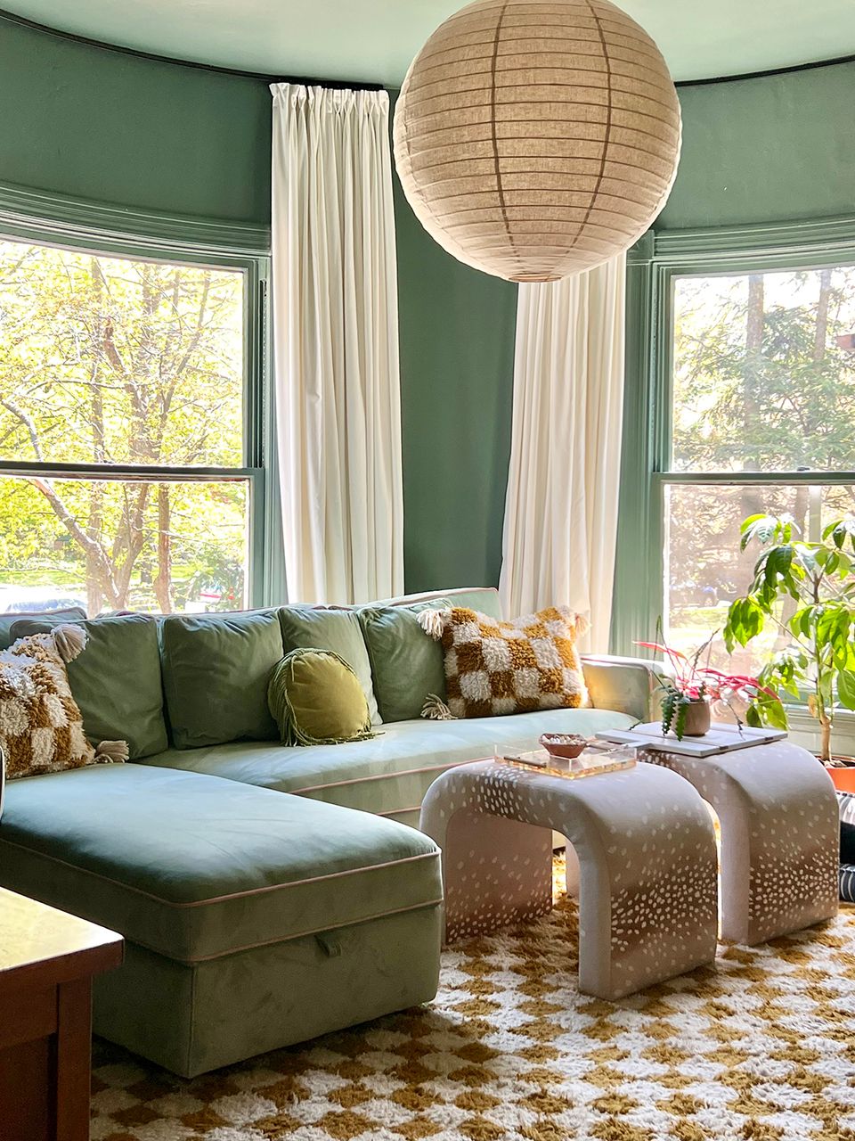 Sage green curved seating with cream curtains, natural pendant light, and earthy botanical aesthetic
