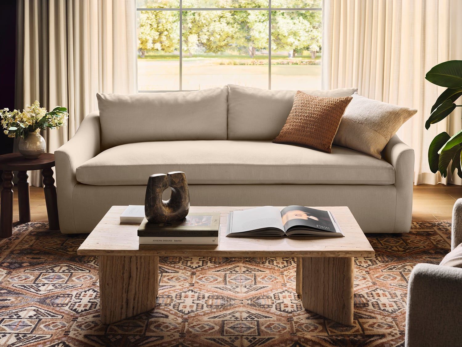 Warm neutral living room with beige sofa, geometric patterned rug, and natural light from large windows