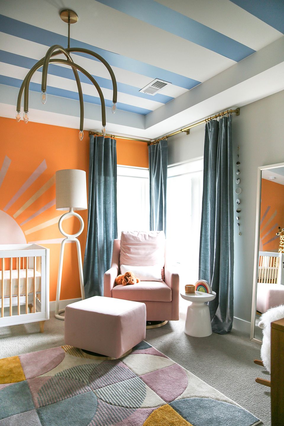 Playful nursery with bold orange accent wall, striped blue ceiling, geometric carpet, and modern pendant light creating energetic yet cohesive atmosphere