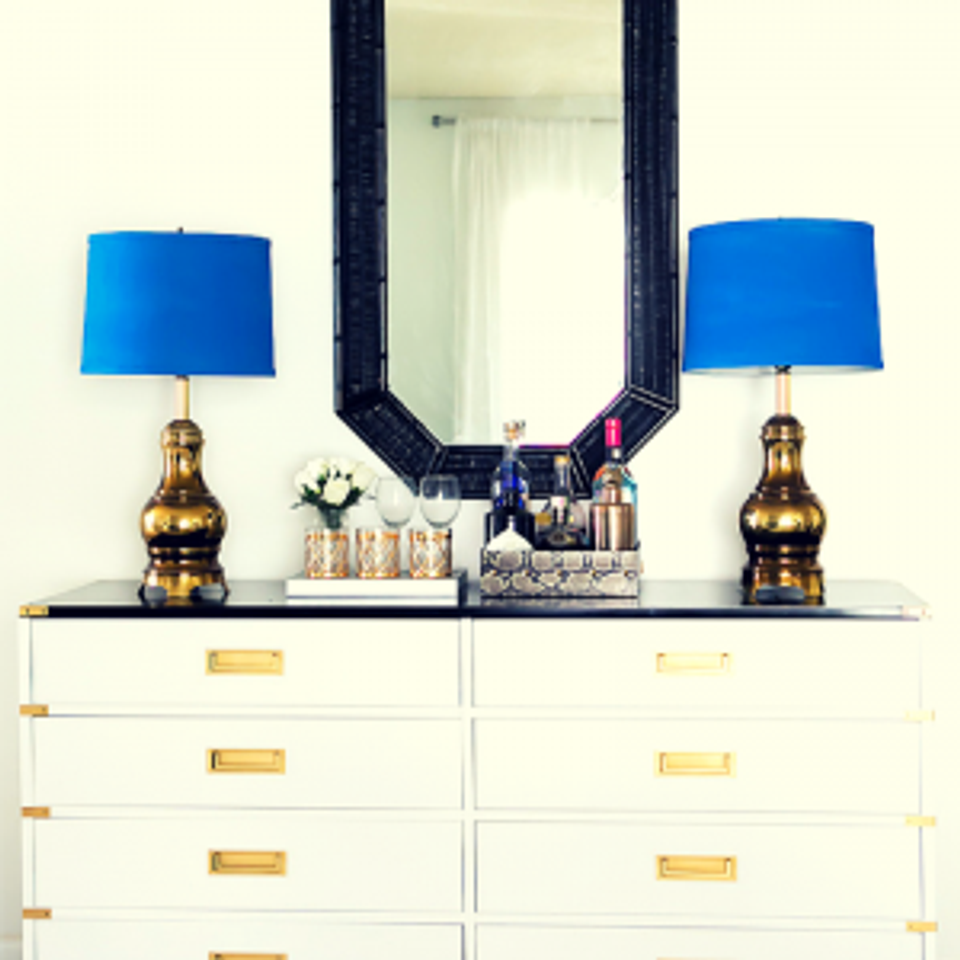 Glam campaign dresser styling with brass accents, cobalt lamps, and navy-framed mirror
