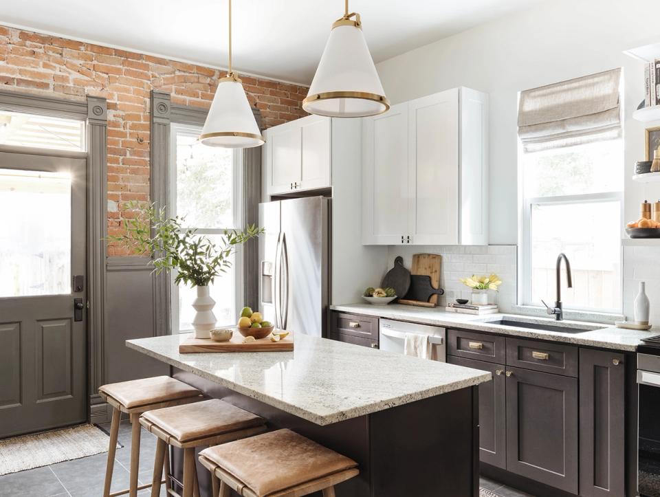 Farmhouse kitchen blending exposed brick, white upper cabinets, dark lower cabinetry, and warm wood accents