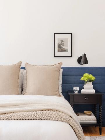Contemporary bedroom with navy blue nightstand, cream bedding, and botanical artwork in minimalist Scandinavian style