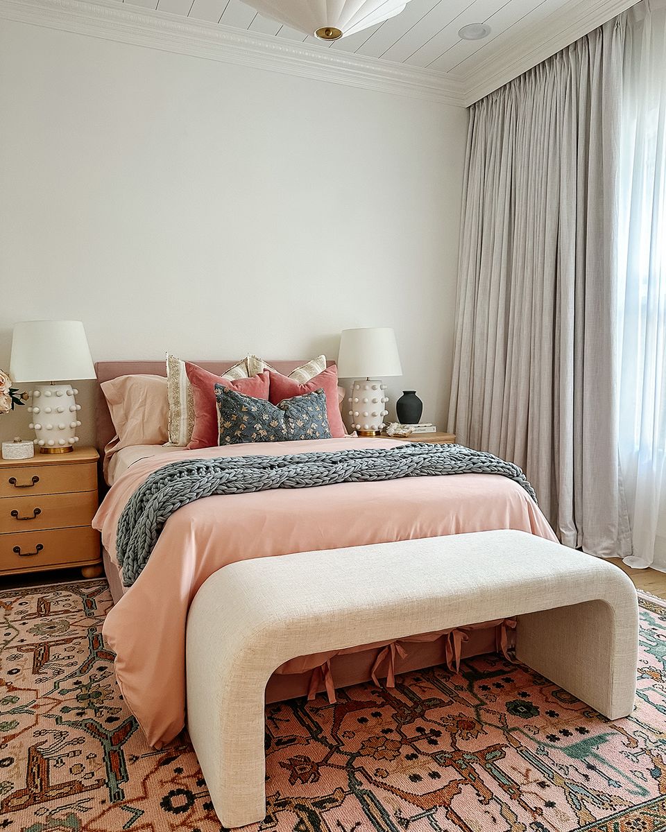 Warm boho bedroom with coral bedding, patterned geometric rug, and mid-century wood nightstands