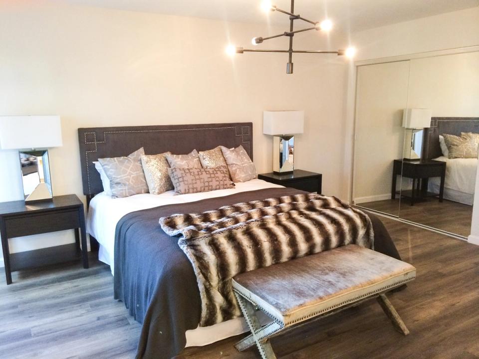 Modern bedroom with dark headboard, striped throw, brass fixture, and minimalist nightstands
