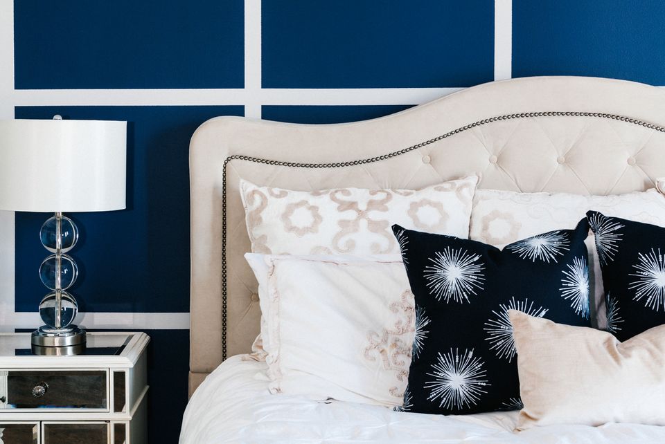 Navy bedroom with crisp white bedding, geometric black pillows, and coastal-inspired nightstand lamp