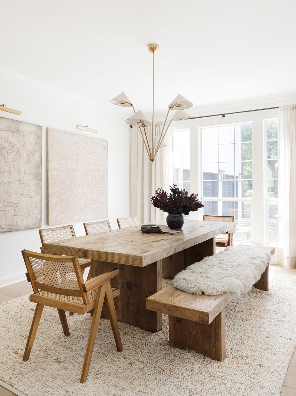 Mid-century modern dining space with natural wood table, caned chairs, brass chandelier, and neutral palette