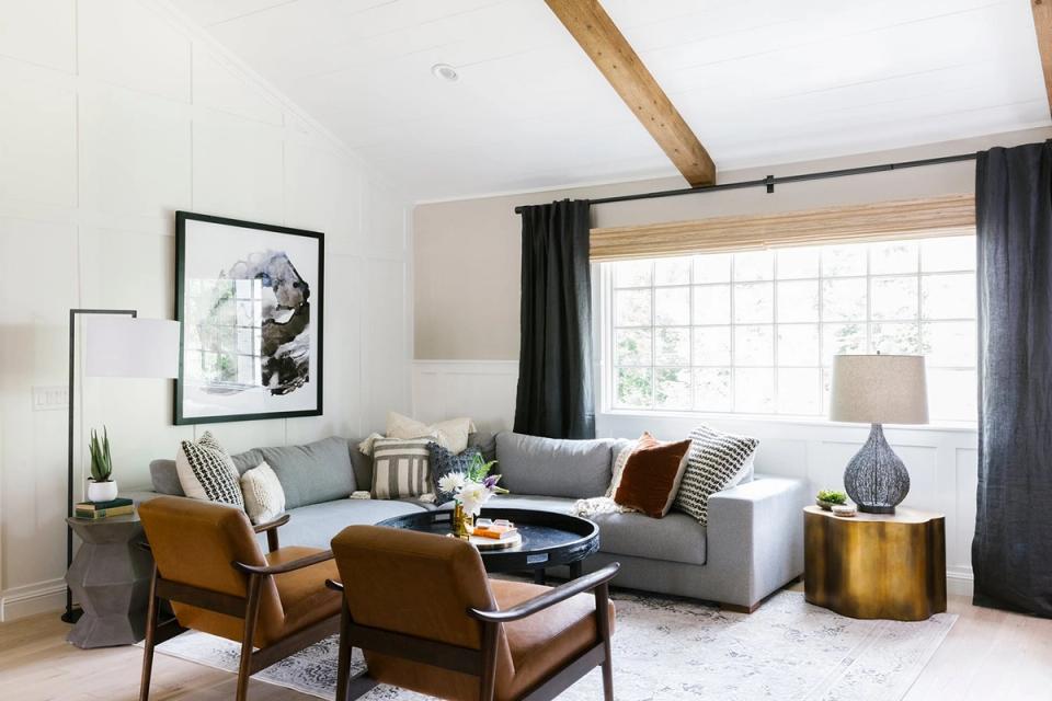 Mid-century modern living room blending warm caramel leather chairs, soft gray sofa, charcoal curtains, and brass accents for layered sophistication