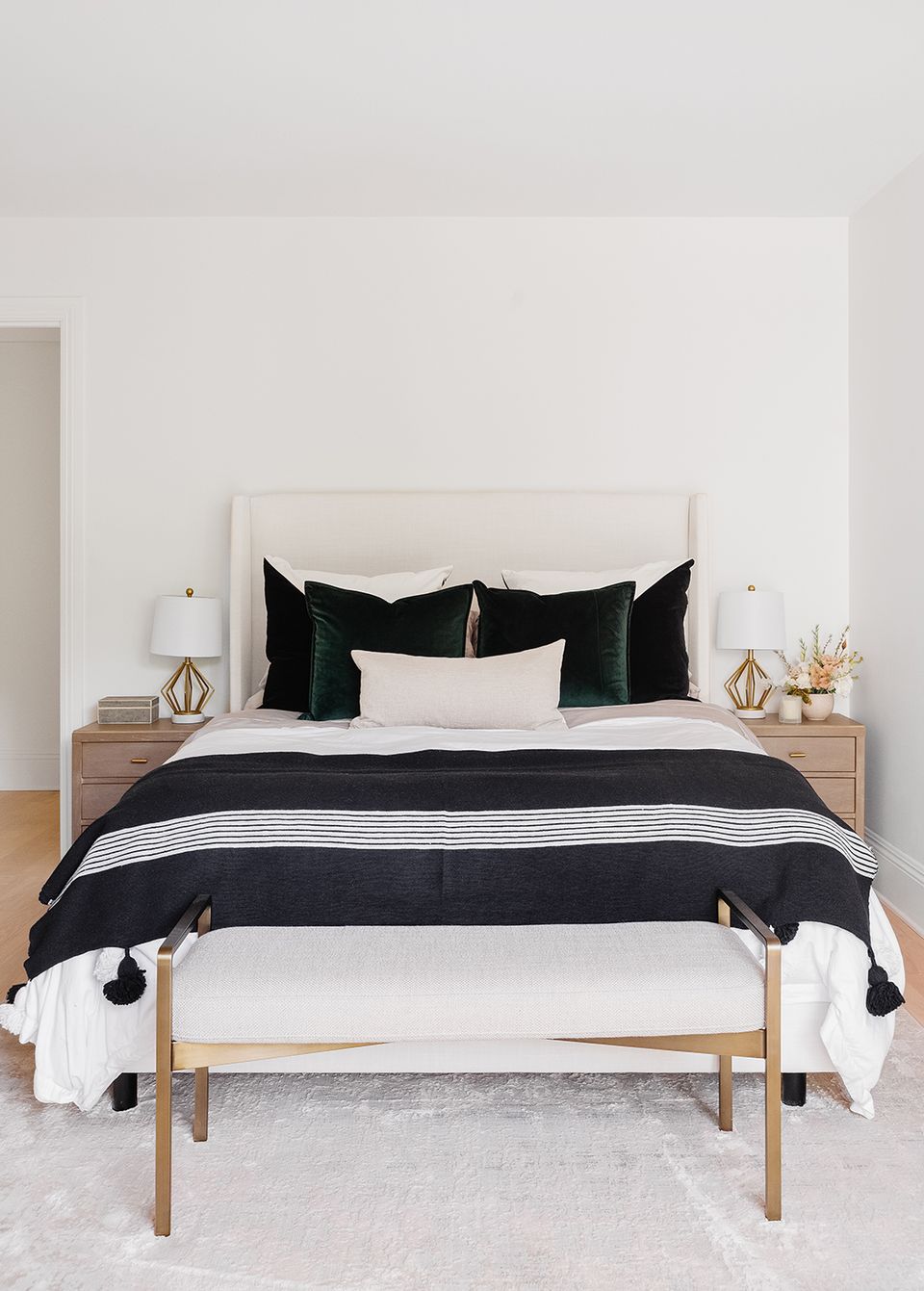 Modern preppy bedroom with black and white striped bedding, cream upholstered headboard, natural wood bench, and clean minimalist styling