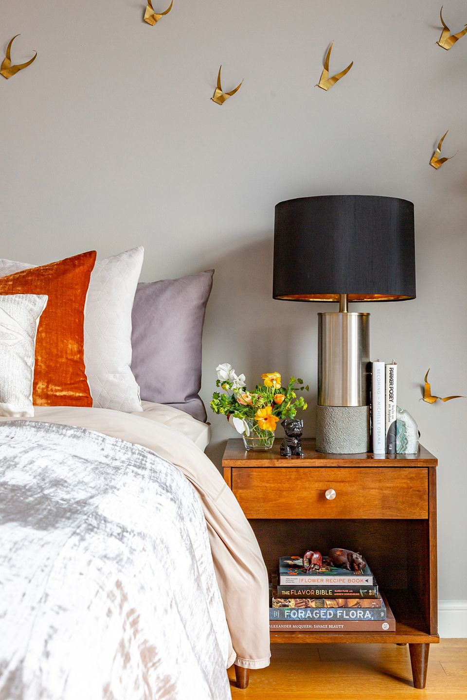 Eclectic bedroom with mid-century modern nightstand, gold paper crane wall decor, and jewel-tone accent pillows