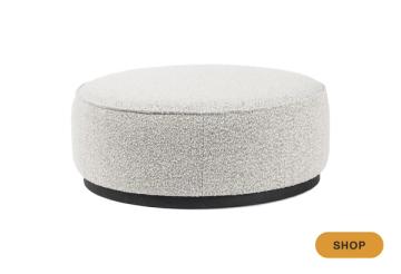 Modern round pouf in cream boucle with black base, minimalist design