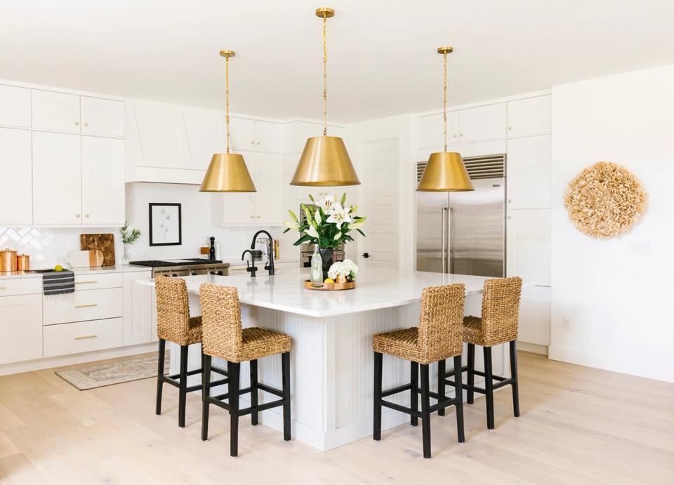 Bright modern kitchen with white island, woven bar stools, and gold pendant fixtures