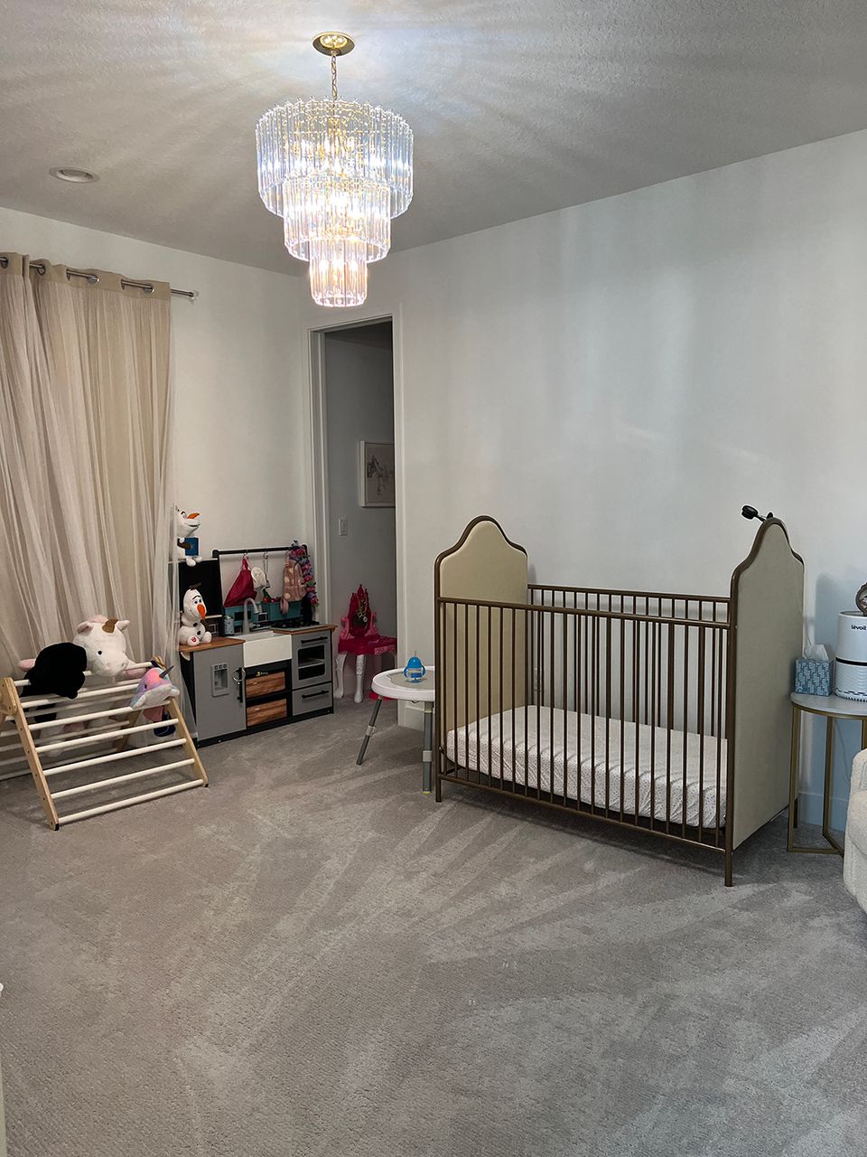 Glam nursery featuring black crib, crystal chandelier, soft gray tones, and modern furnishings