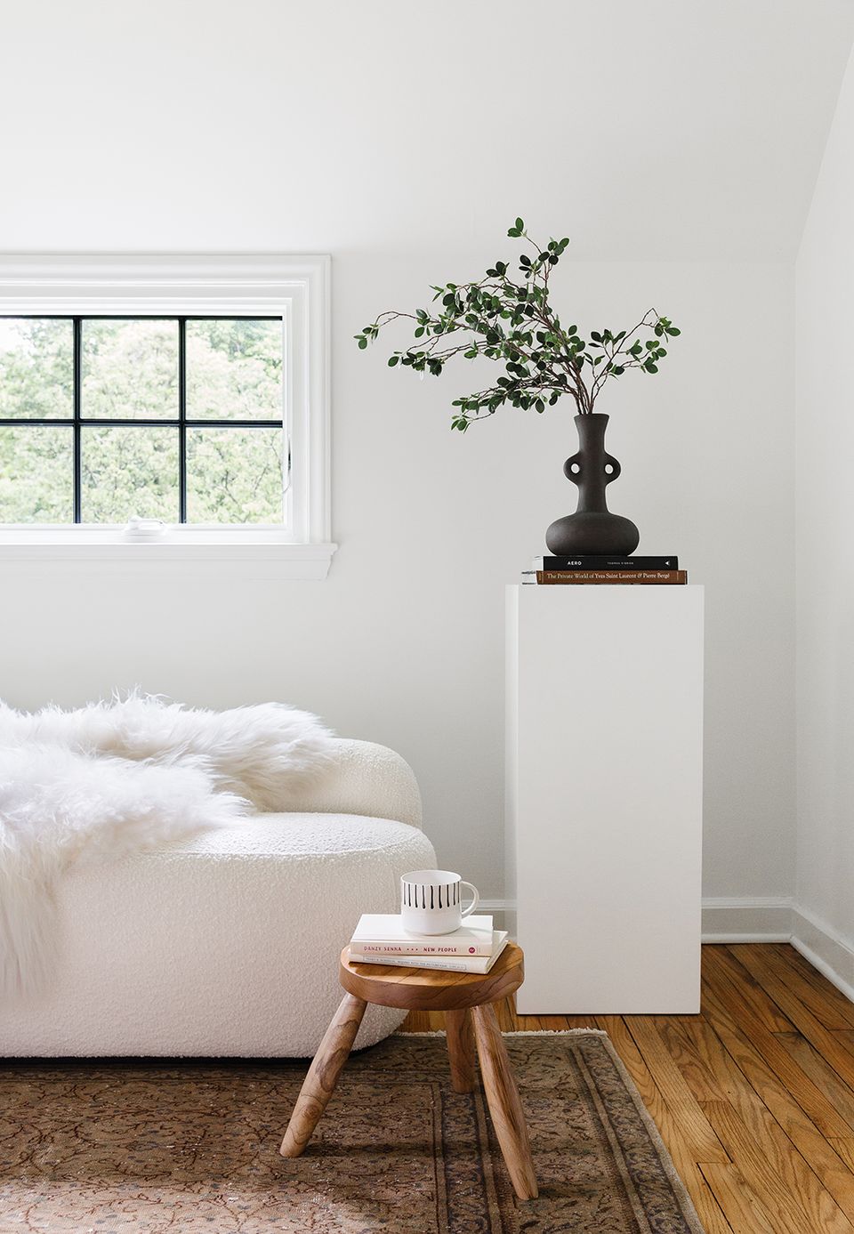 Serene minimalist bedroom with crisp white bedding, natural wood stool, and sculptural black vase