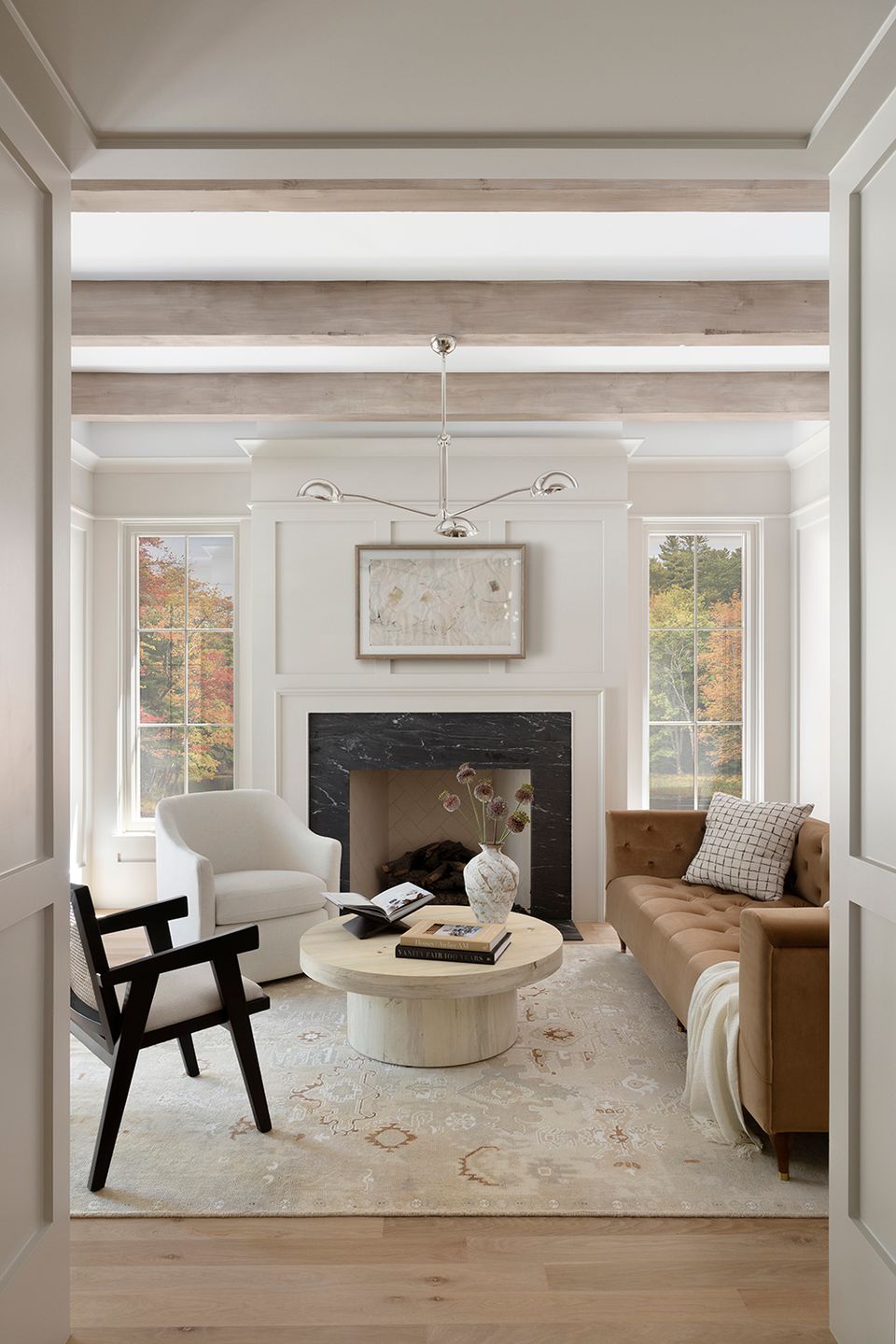 Sophisticated neutral living room with fireplace, monochromatic beige palette, mid-century modern accents, and abundant natural light from tall windows.