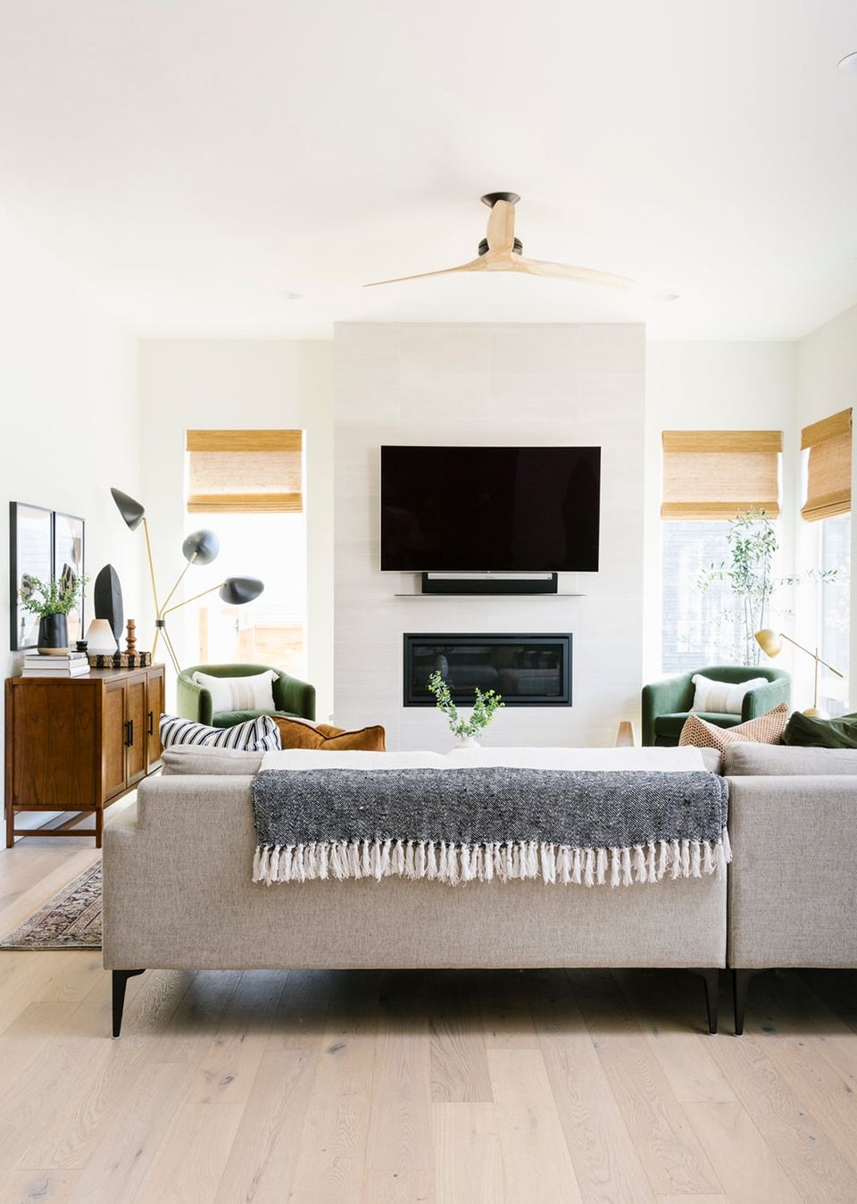 Minimalist modern living room with floating TV above fireplace, neutral palette, natural wood accents, and light-filled contemporary design