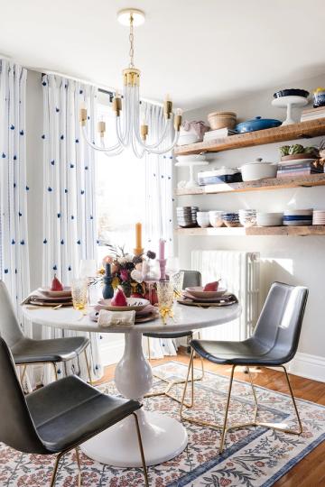Contemporary dining nook with floating wood shelves, round pedestal table, patterned curtains, and brass chandelier