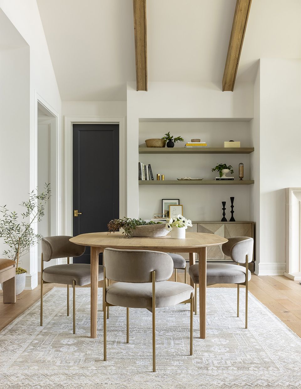 Scandinavian dining space with light wood round table, neutral upholstered chairs, and minimalist shelving