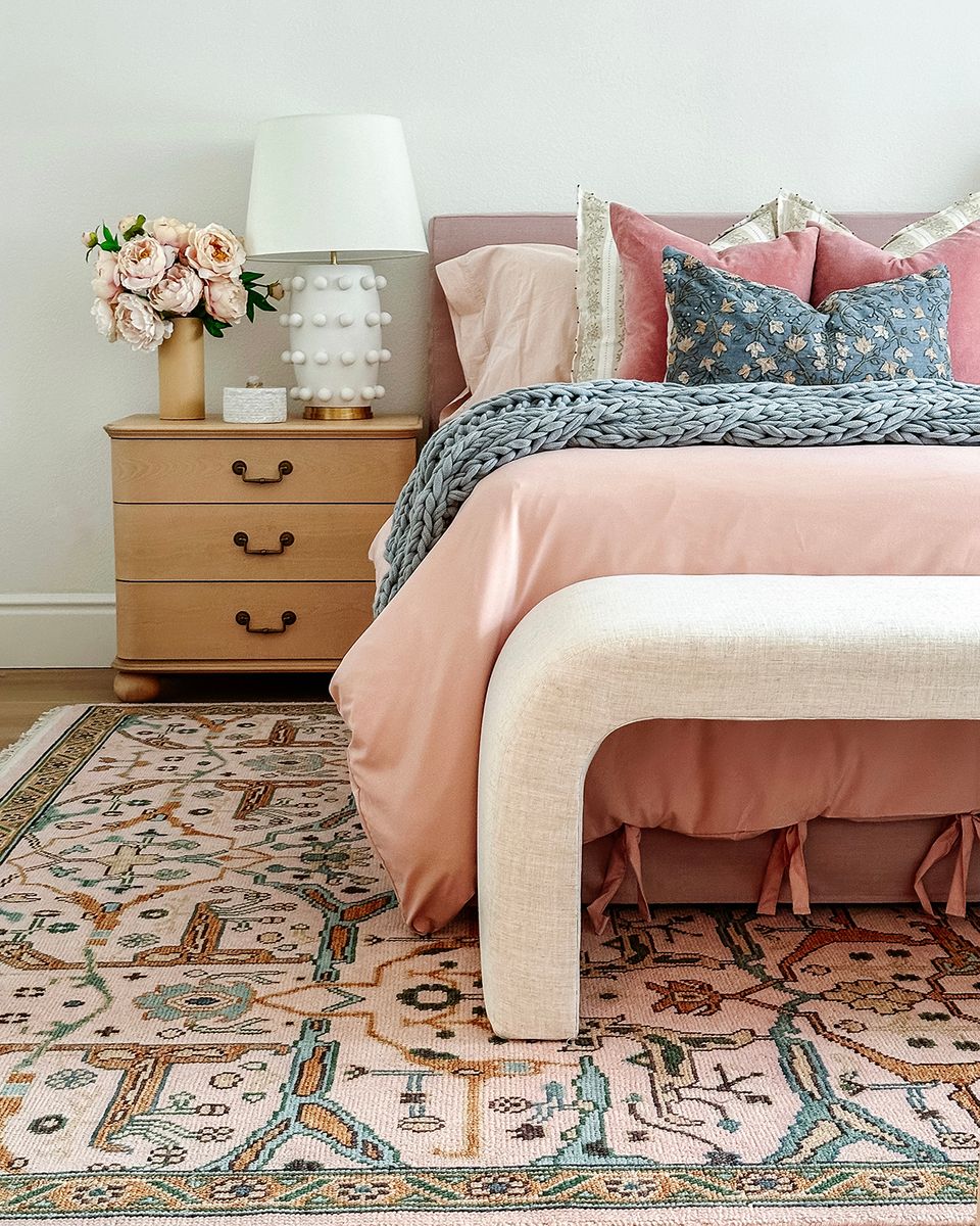 Romantic maximalist bedroom with blush bedding, patterned rug, and soft wood tones