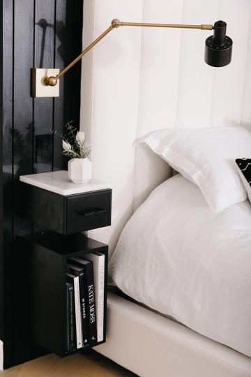 Scandinavian bedroom with black floating nightstand, brass articulating sconce, and crisp white bedding