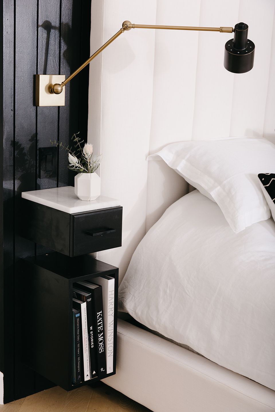 Scandinavian bedroom with black floating nightstand, brass articulating sconce, and crisp white bedding