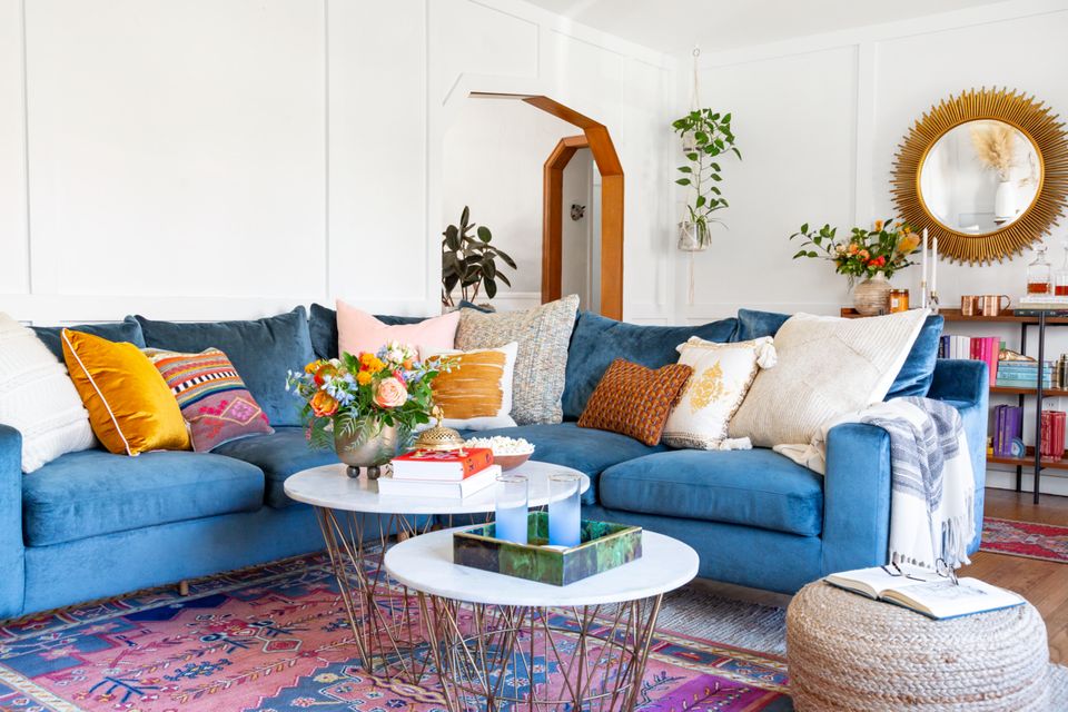 Eclectic living room with blue sectional, hanging plants, colorful pillows, and bohemian rug