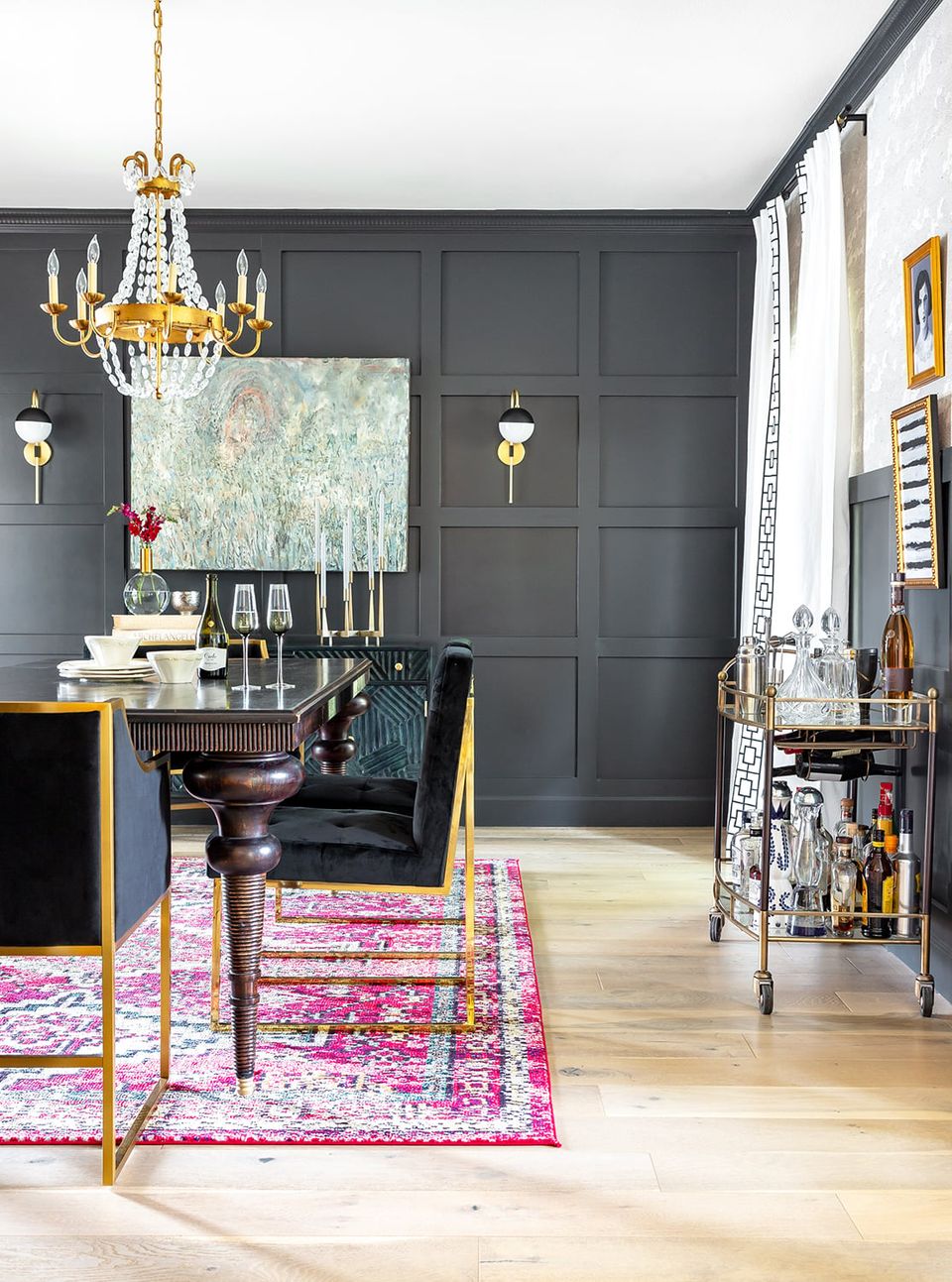 Eclectic dining room with dark charcoal walls, gold chandelier, fuchsia area rug, and moody sophisticated atmosphere
