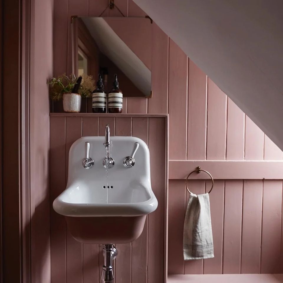 Modern farmhouse bathroom with dusty rose paneled walls, white pedestal sink, and minimalist shelving in soft pink tones