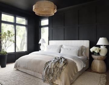 Dramatic modern bedroom with black walls, white bedding, layered neutral pillows, and warm wood nightstands creating moody luxury