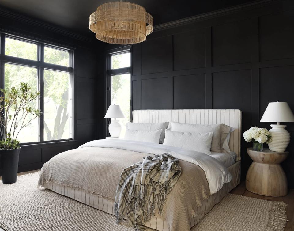 Dark dramatic bedroom with black walls, white upholstered headboard, natural wood accents, and woven ceiling fixture for moody elegance