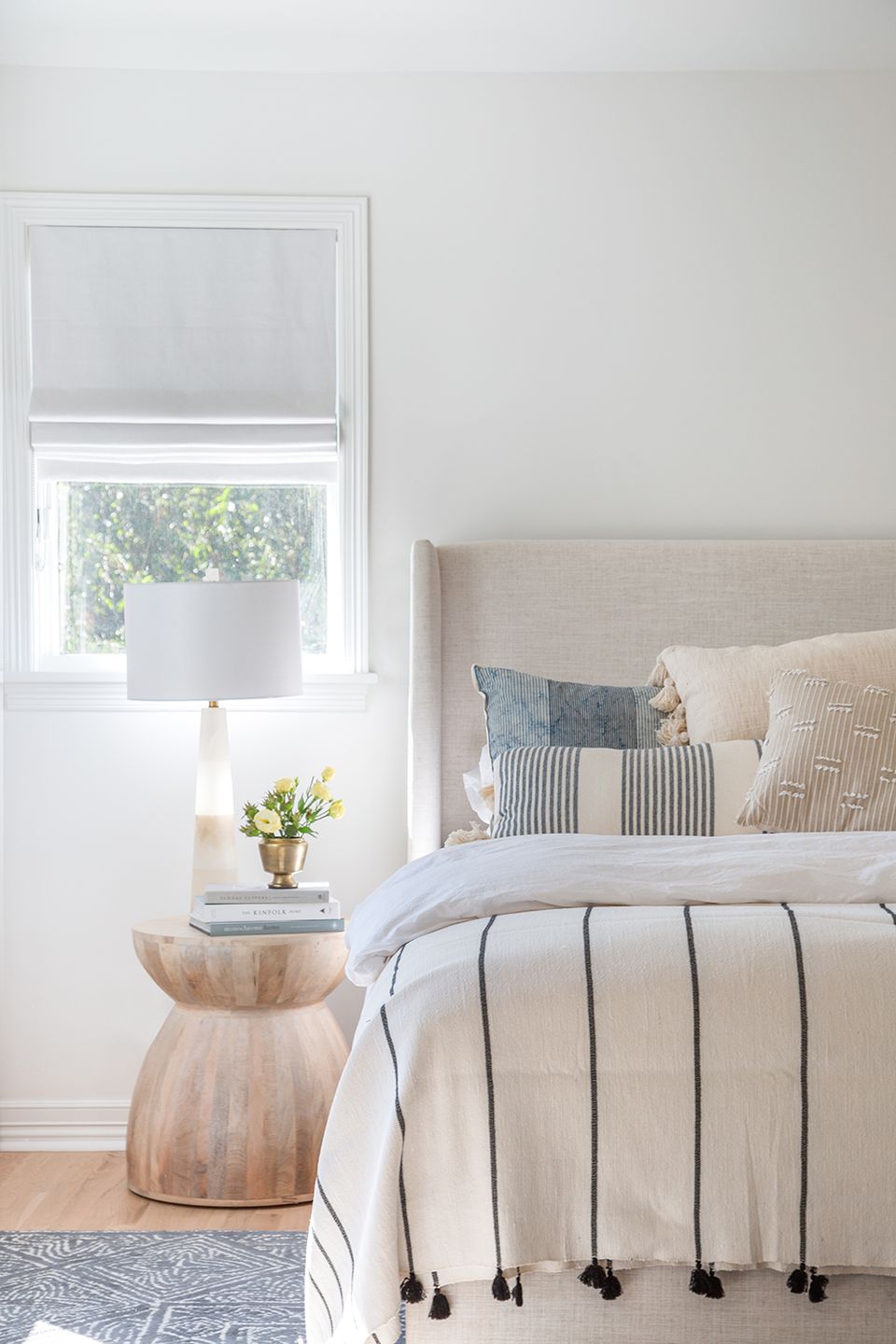 Minimalist bedside with natural wood pedestal table, soft linen, and abundant natural light